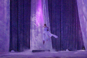 two acrobat performers up in the air on cloth ropes with a purple hues of light all over the stage and low lying fog on the stage floors with abstract gobo patters on the three white curtains Gabriel's Christmas Story, Calvary Orlando, Winter Park, Florida, USA
